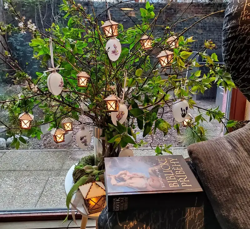 sklenené veľkonočné vajíčka a drevené lampášiky zavesené na vetvičke vo váze